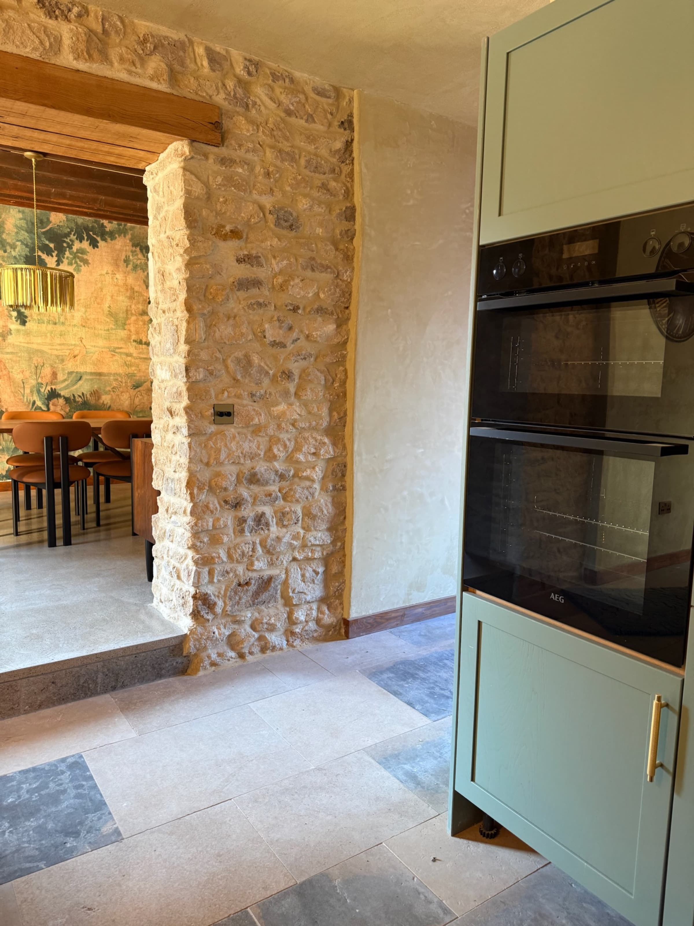 Kitchen opening through stone arch to tapestry dining room