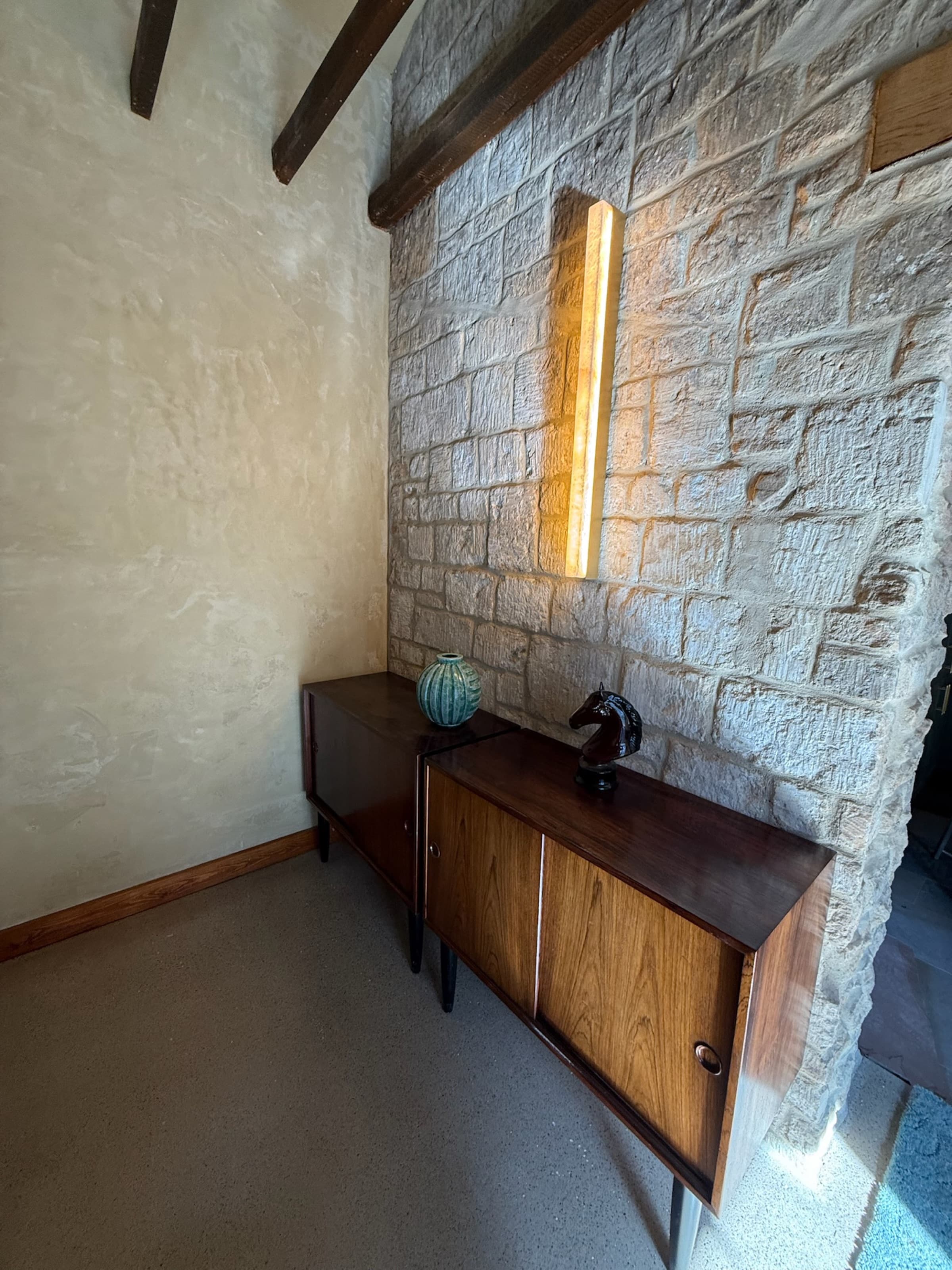 Lounge corner, exposed stone wall, mid-century sideboard, brass linear light